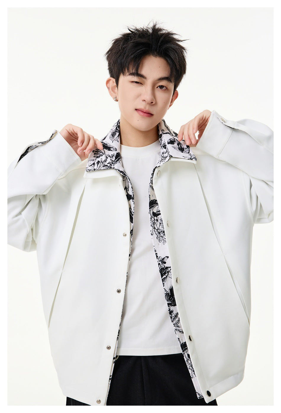 Model wearing a white snap-front jacket with black floral-print collar and trim, shown over a white shirt.