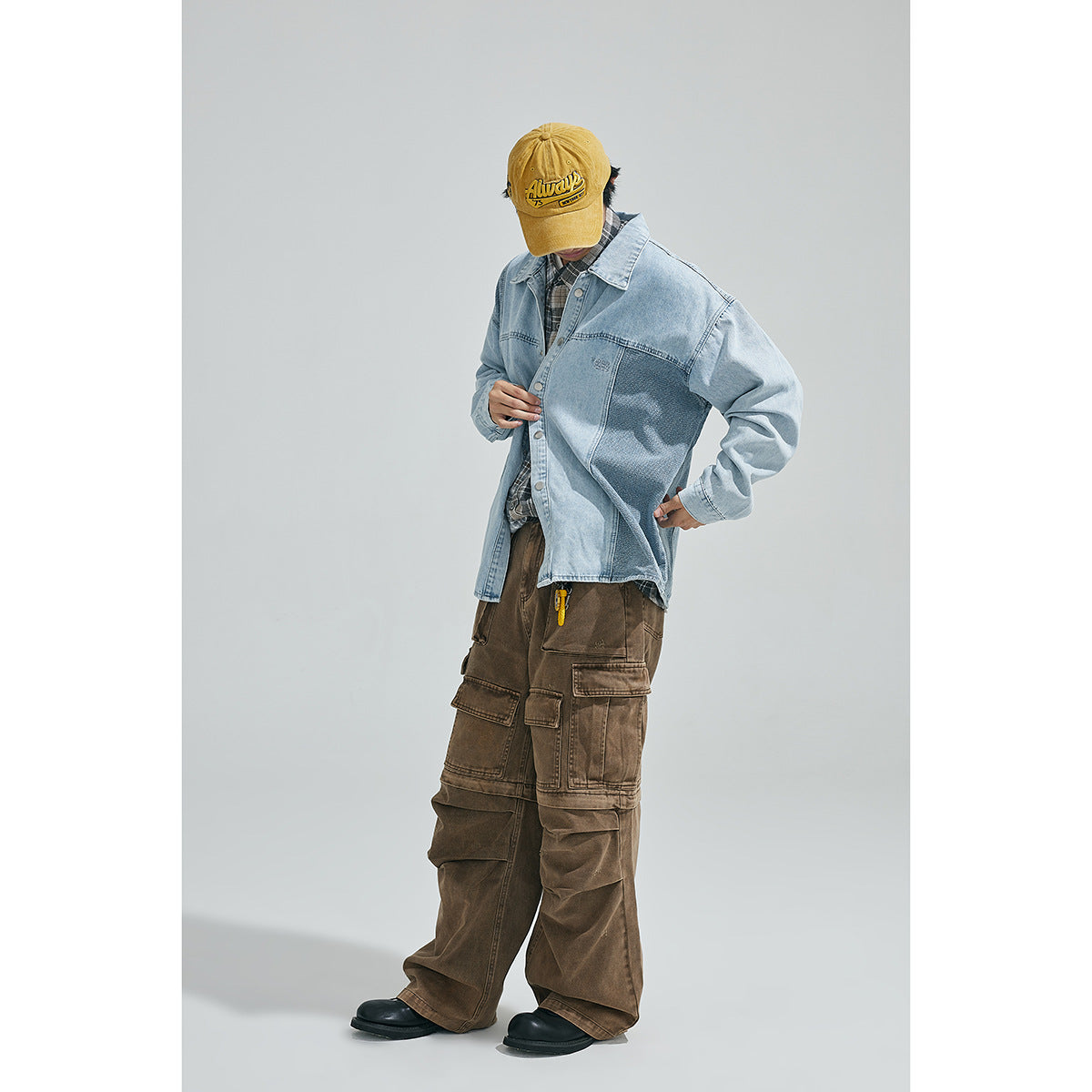 Full-length model wearing a light-blue contrast-panel denim jacket, plaid shirt, brown cargo pants and yellow cap.