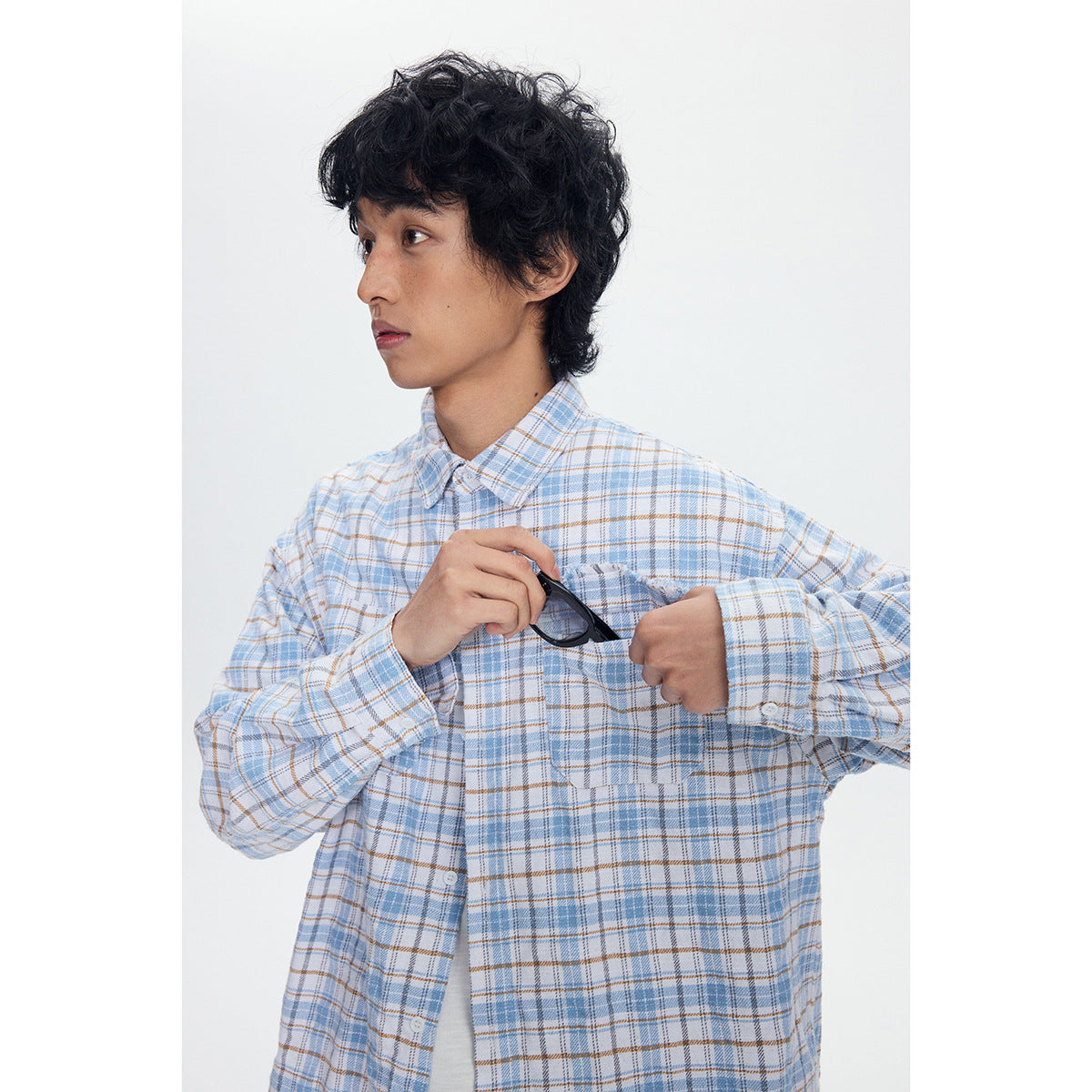 Close view of a blue-and-tan plaid shirt with chest pockets as the model holds sunglasses above one pocket.