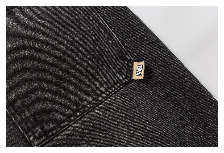 Close-up of charcoal denim with a rear pocket seam and a small tan sewn label.