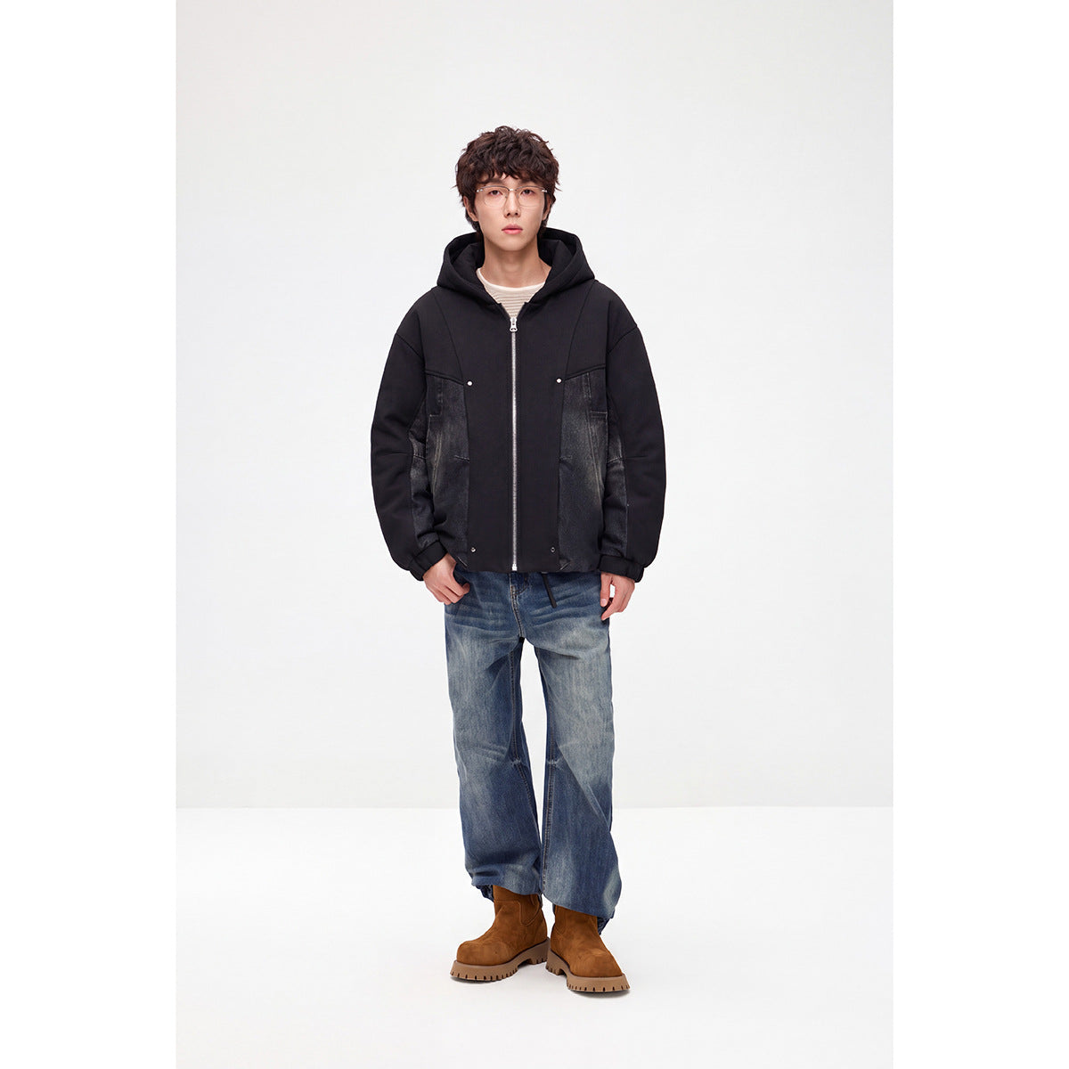 Model wearing a black hooded zip jacket with dark denim panels, shown from the front.