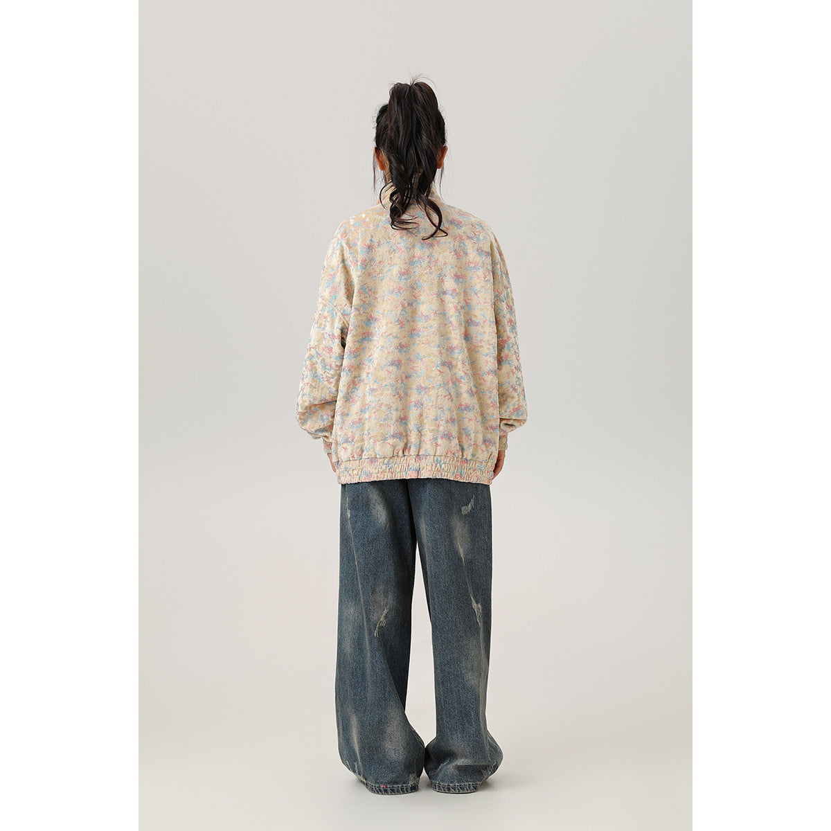 Back view of a model wearing a pastel multicolor jacket with elastic cuffs and hem.