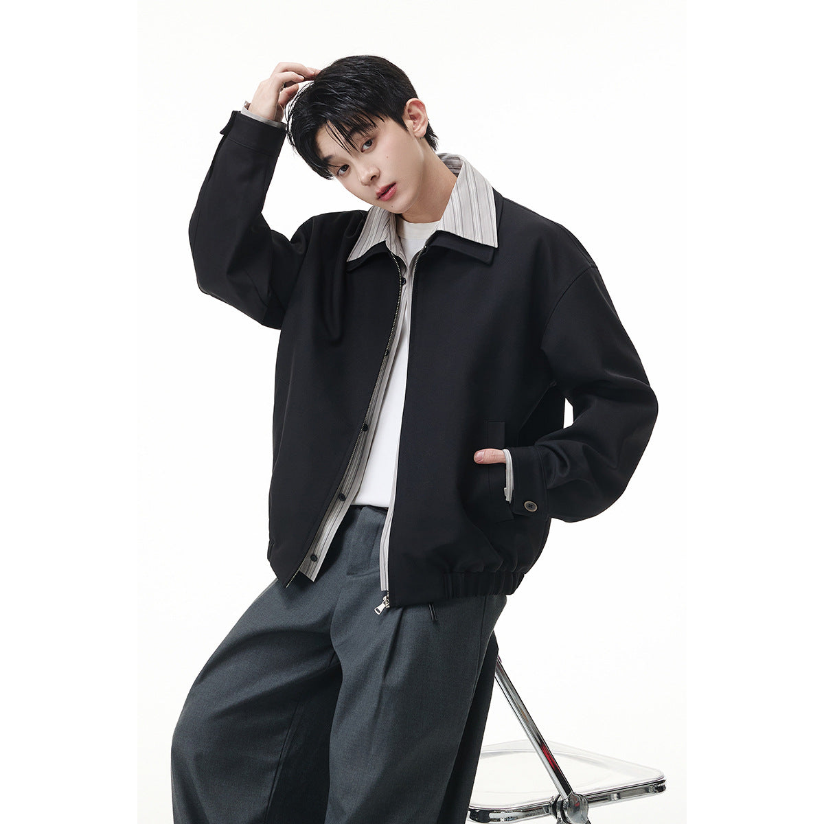 Model wearing a relaxed black zip-front jacket with a wide collar, layered over a light striped shirt.