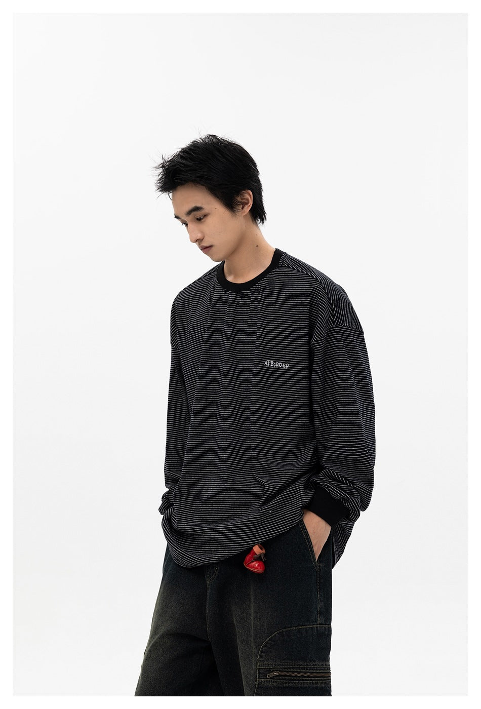 Model wearing black striped long-sleeve top with embroidered chest lettering, looking down, hand in pocket of dark pants