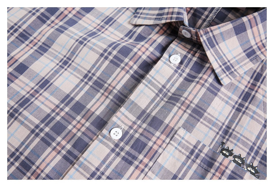 Close-up of a pale blue-gray and blush plaid shirt front, with white buttons and a chest pocket featuring black cats.