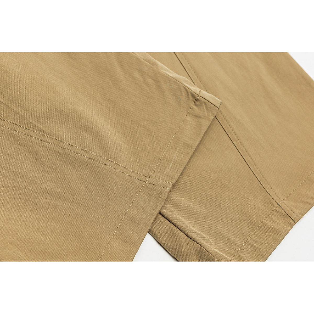 Close-up of tan pants showing overlapping leg panels, stitched seams, and a folded hem.
