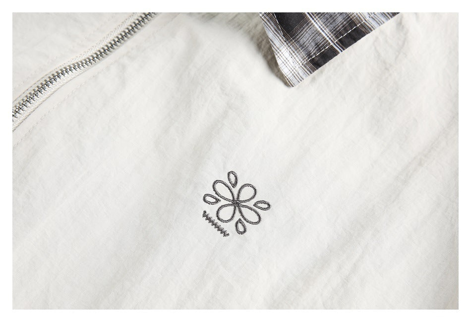 Close-up of a small dark embroidered flower motif on light beige fabric, with plaid fabric at the edge.