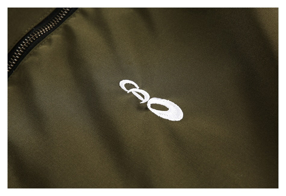 Olive jacket close-up showing a small white embroidered emblem beside the zipper.