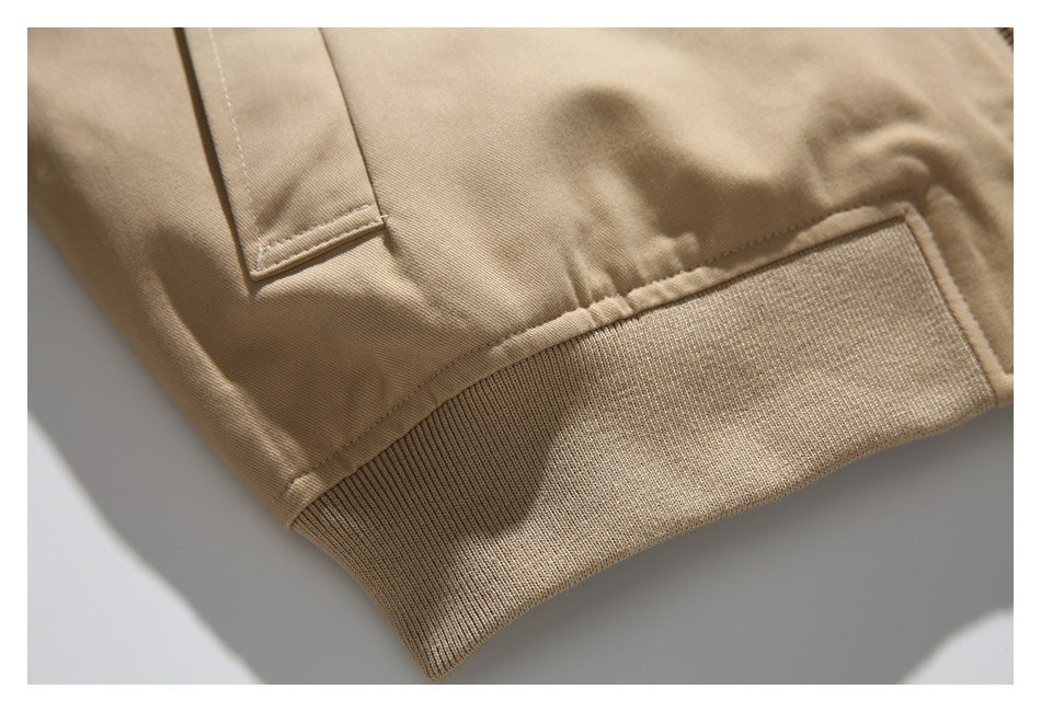 Close-up of a tan jacket showing its ribbed hem, seam, and edge of a welt pocket.