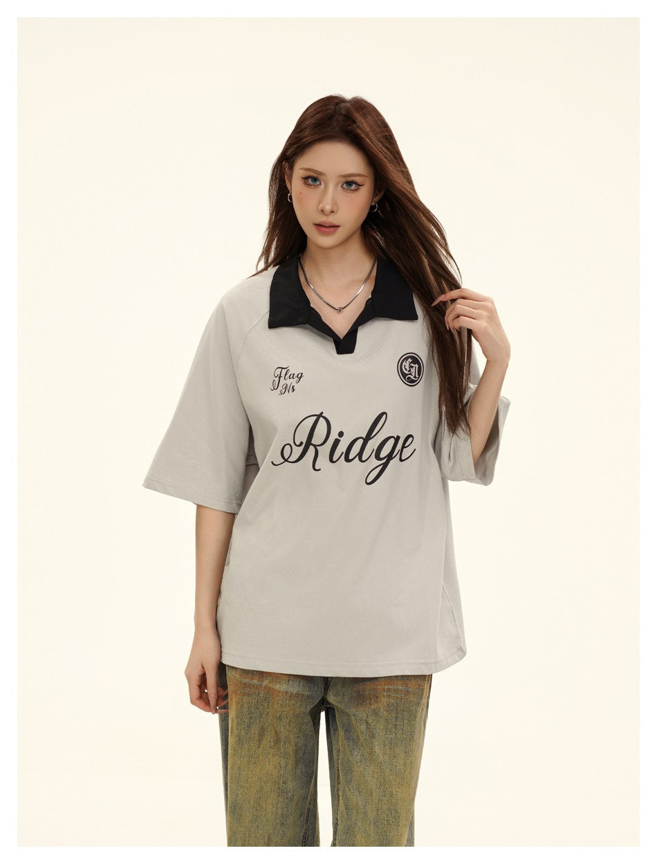 Front view of a model in a light gray oversized polo with black collar and lettering, with faded jeans.