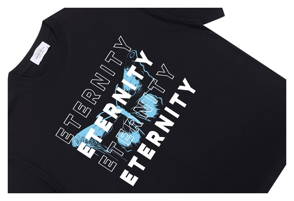 Black T-shirt laid flat at an angle, with a large blue-and-white layered “ETERNITY” graphic on the front.
