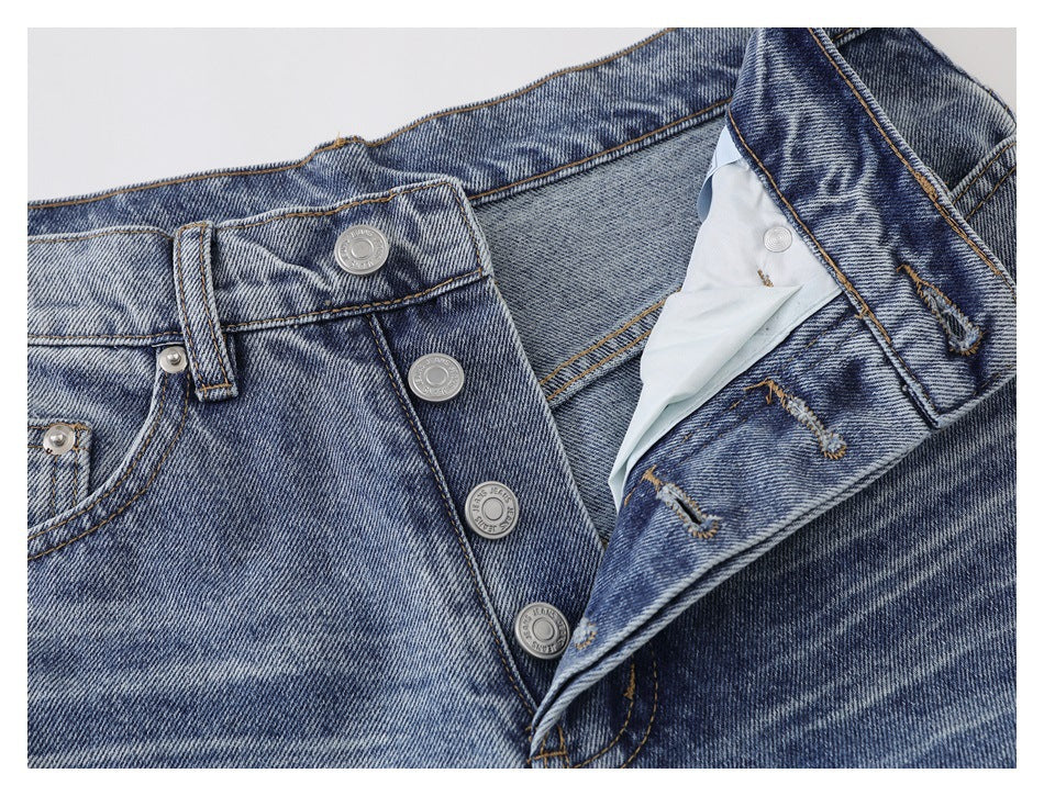 Close-up of faded blue jeans with the fly open, showing a button closure, belt loop and front pocket.