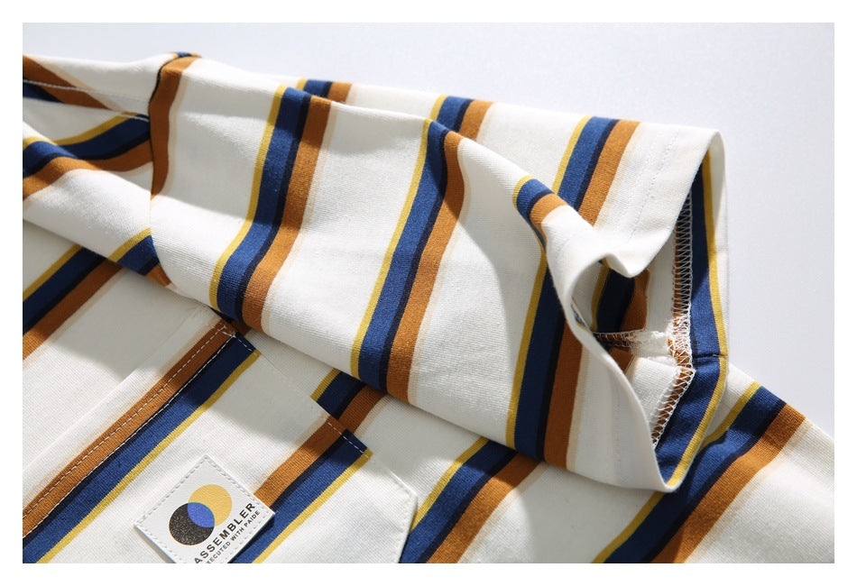 Close-up of the cream T-shirt’s striped sleeve and stitched hem beside the chest pocket.