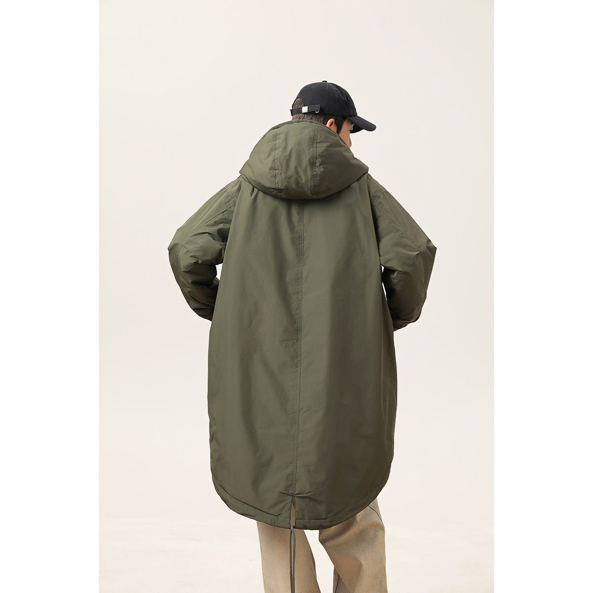 Rear view of a model wearing a long dark olive parka with a large hood and rounded hem.