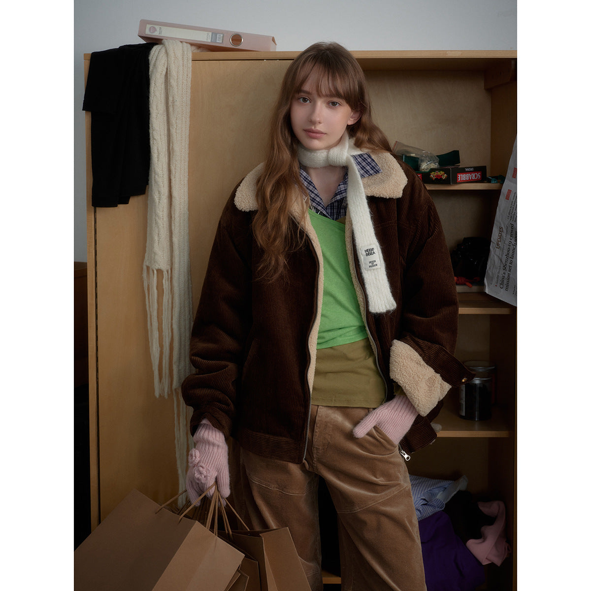 Model wearing a dark brown corduroy jacket with cream sherpa collar and cuffs, layered over a green top.
