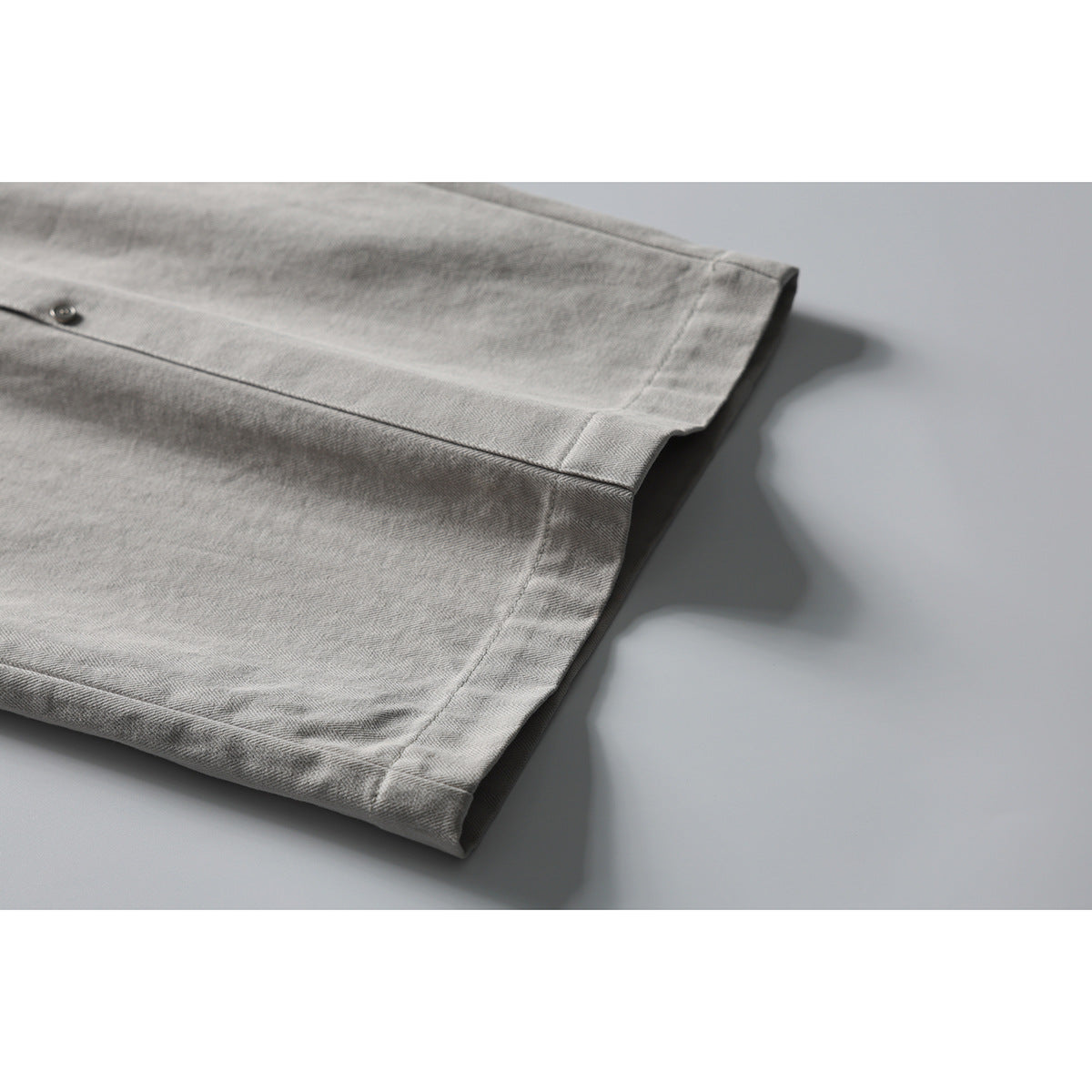 Close-up of the hem and stitching on light gray herringbone trousers.