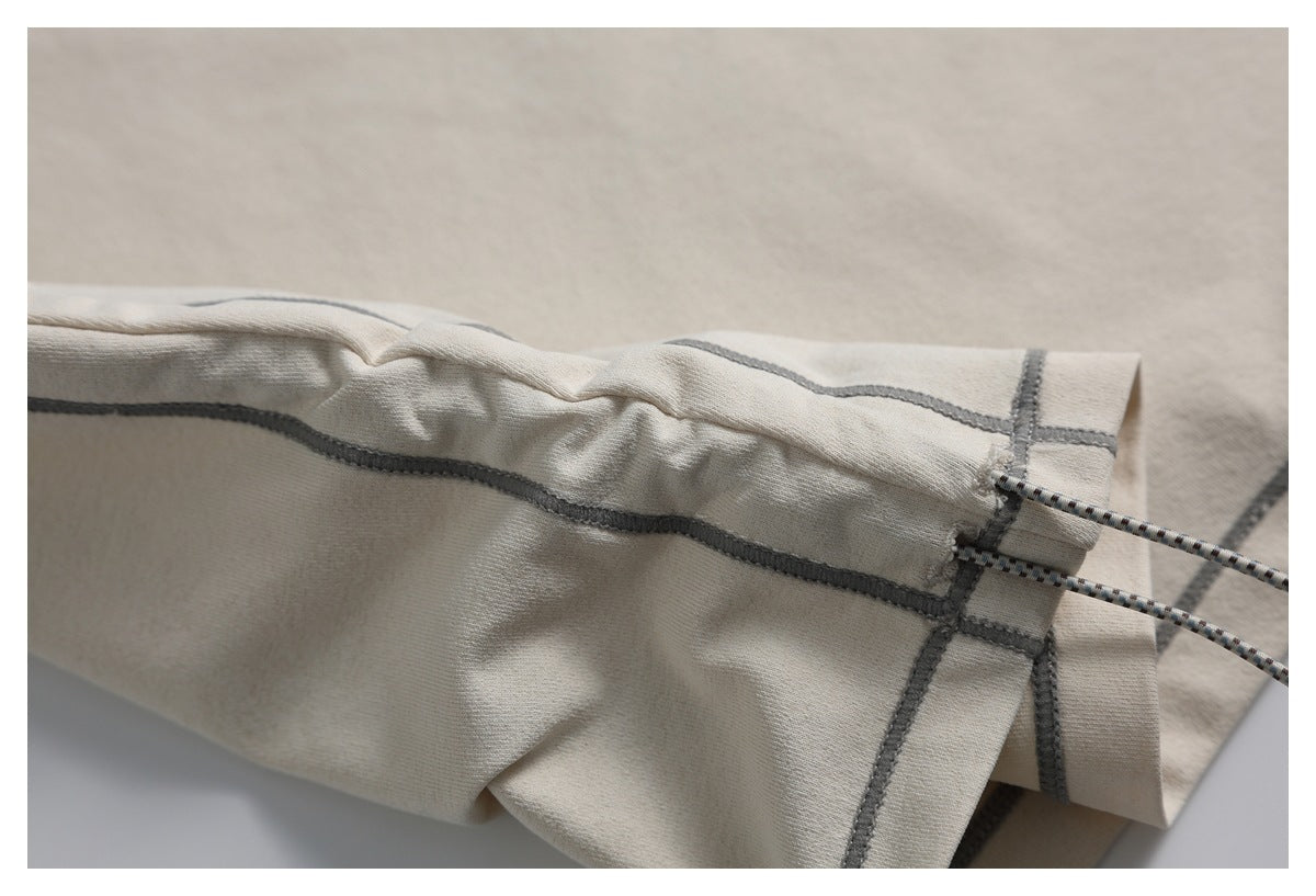 Close-up of a gathered light beige hem with gray stitching and an adjustable cord.