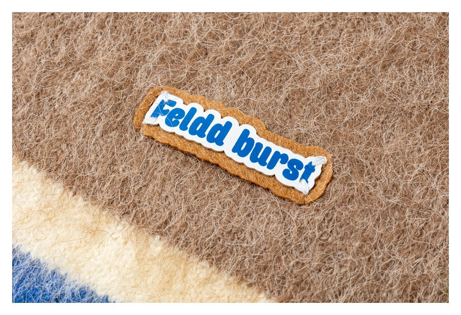 Close-up of the vest's fuzzy brown knit and sewn-on brand patch above a cream and blue stripe.