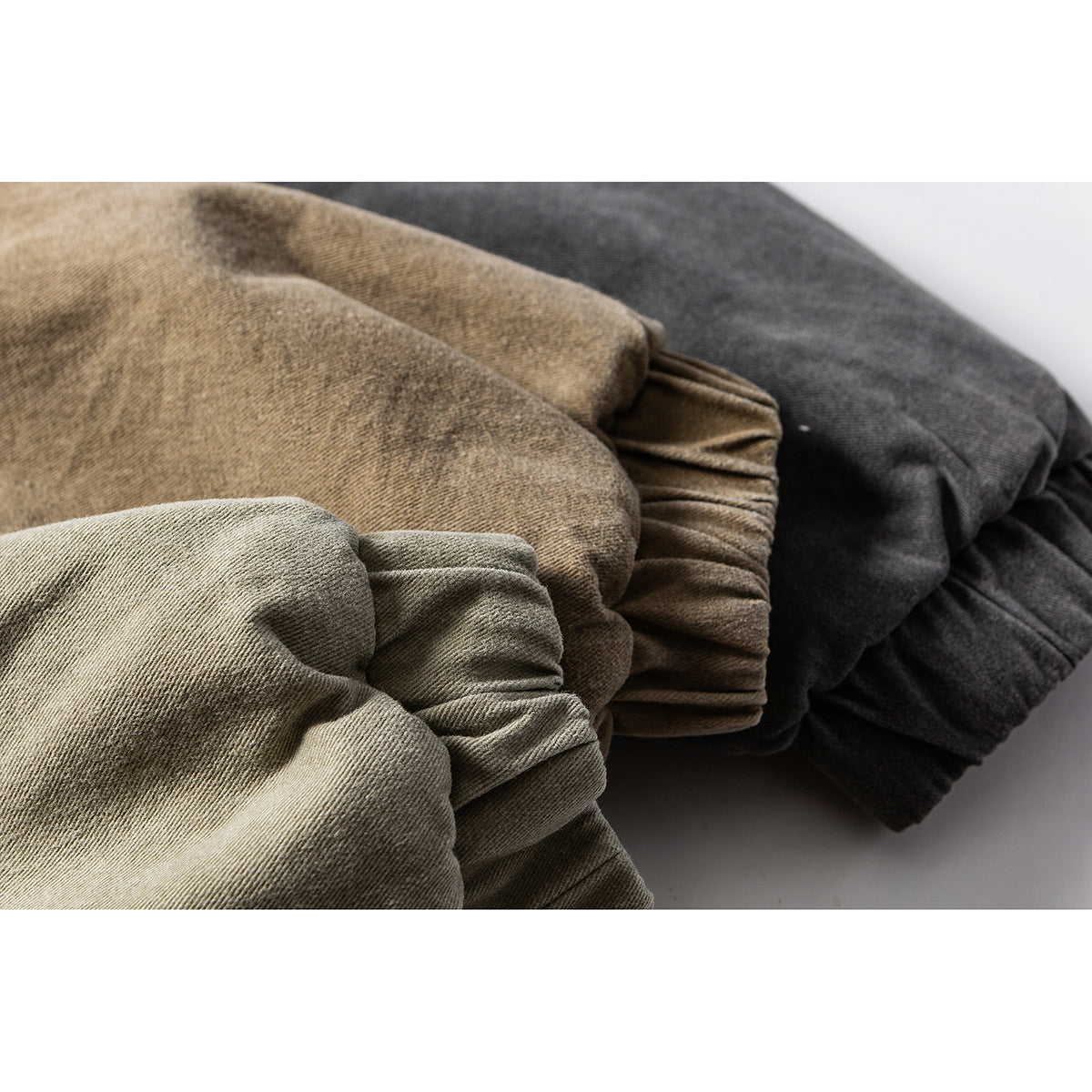 Close-up of folded jacket fabric in light olive, brown, and charcoal colors, showing its surface and gathered cuff.