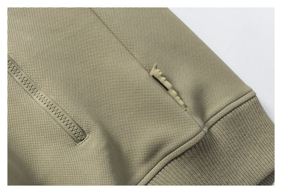Close-up of an olive jacket pocket zipper, a small fabric detail, and a ribbed cuff.