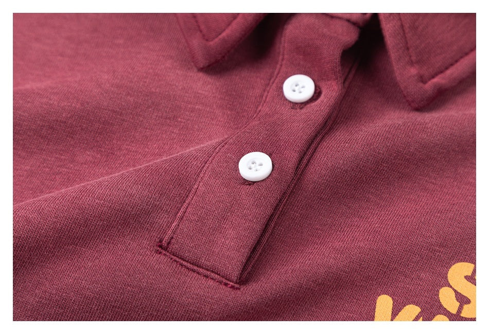 Close-up of a burgundy collared top with two white buttons and part of a yellow printed graphic.