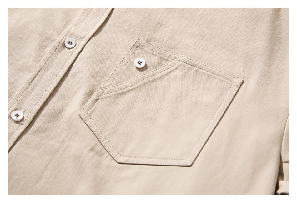 Close-up of a beige shirt's button placket and angular chest pocket with a white button.