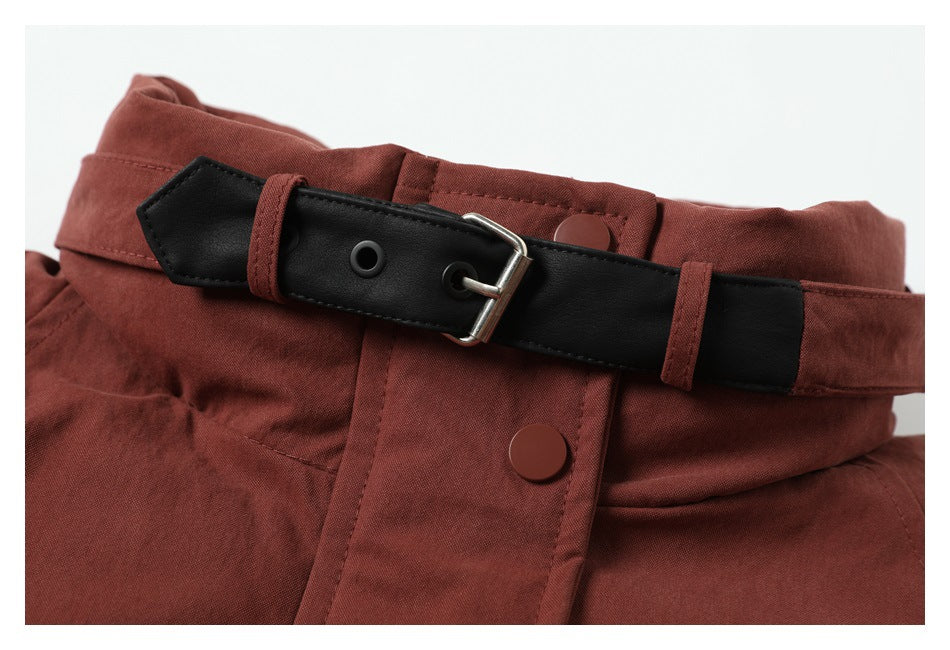 Close-up of a rust-red garment waist with a black belt, metal buckle, belt loops and snap closure.