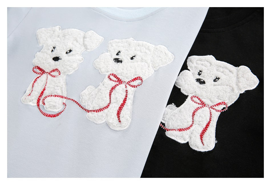 White teddy bear appliqué with red stitched accents shown on pale blue and black tops.