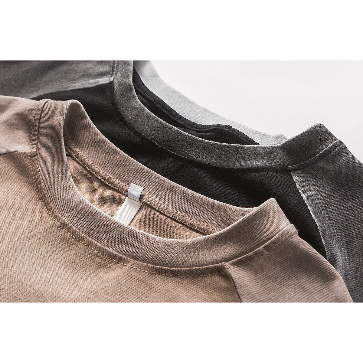 Close-up of taupe and charcoal raglan T-shirts showing their ribbed crew necklines and stitching.