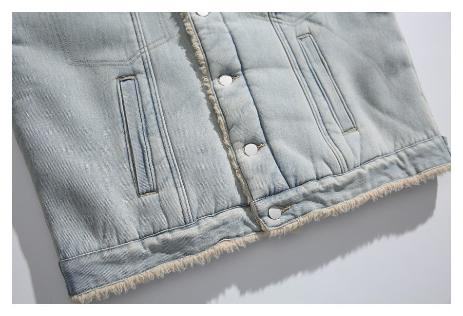 Close-up of a light-wash denim jacket with front pockets, silver snaps, and cream fringe along the hem.