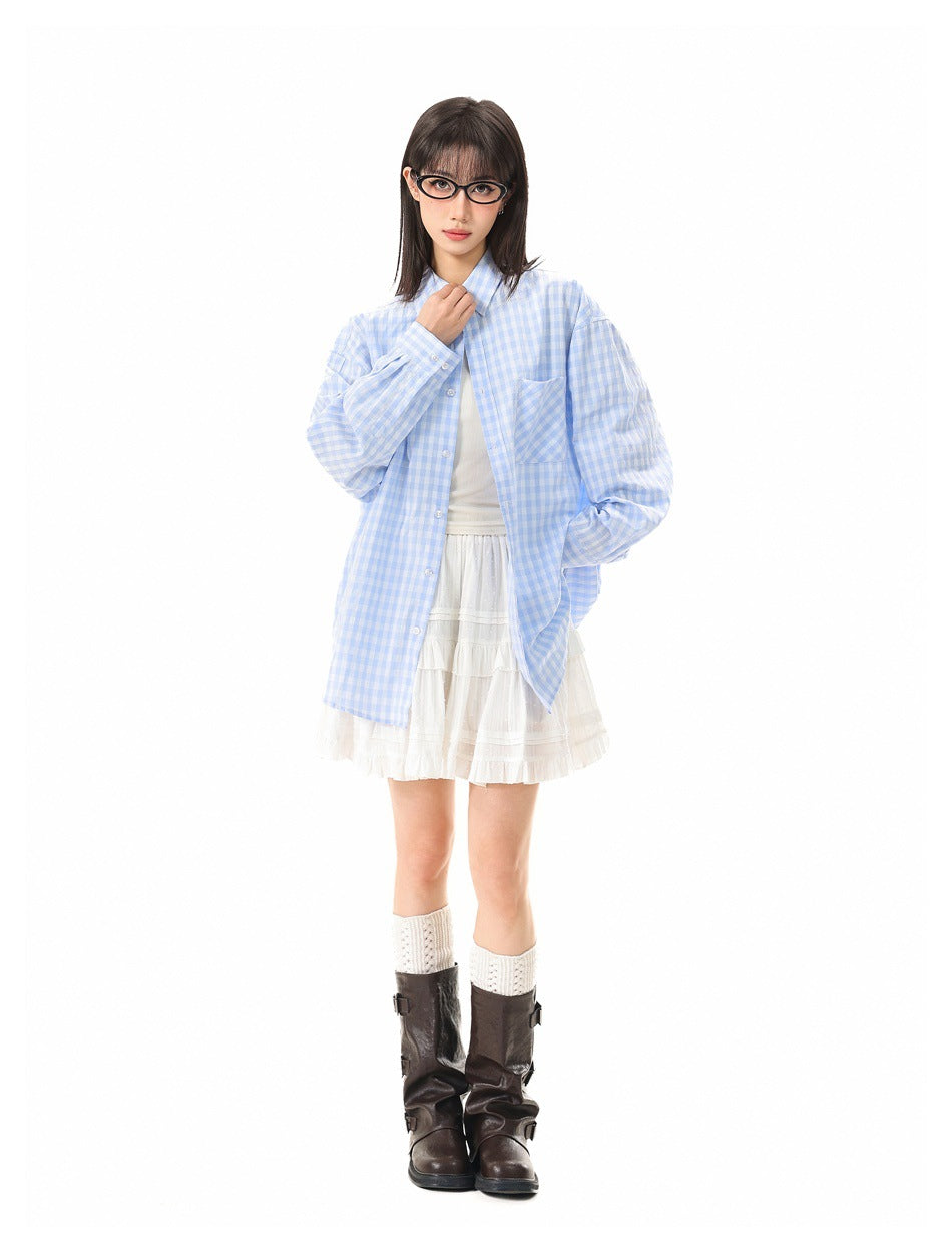 Model wearing an oversized light blue and white gingham shirt over a white tiered skirt, with dark brown boots.