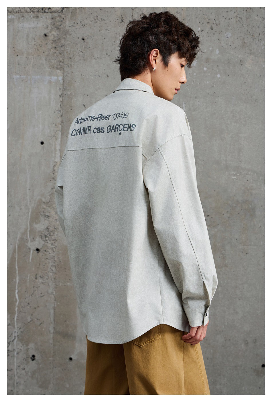Back view of a model wearing a light gray oversized shirt with dark text printed across the shoulders.