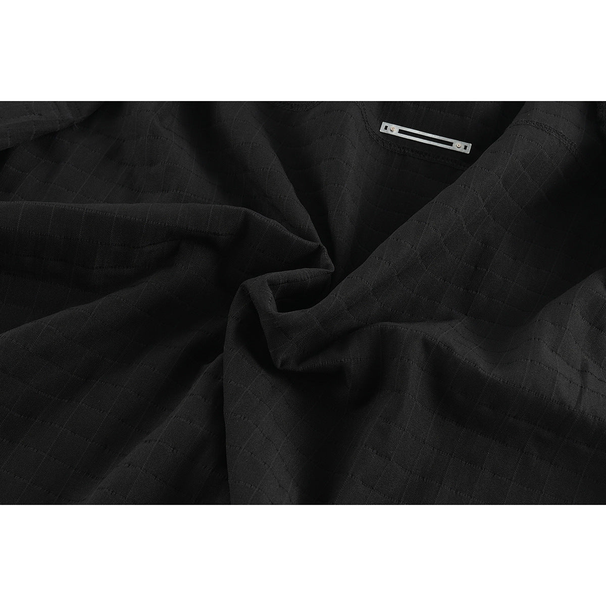 Close-up of black shirt fabric gathered to show its subtle grid-like texture and a small metal detail.
