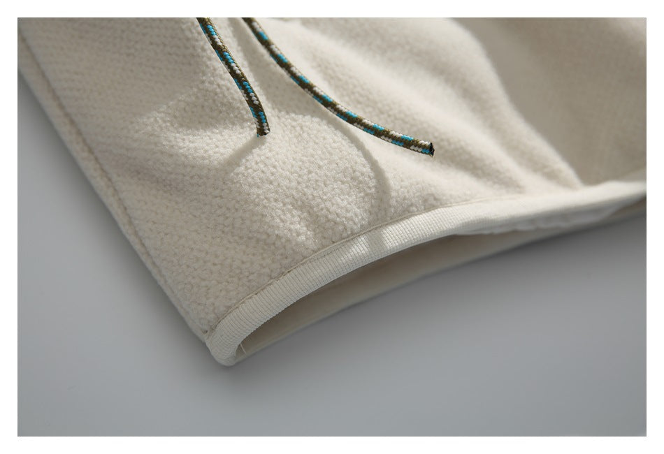 Close-up of multicolored cords and a bound hem on a cream textured garment.