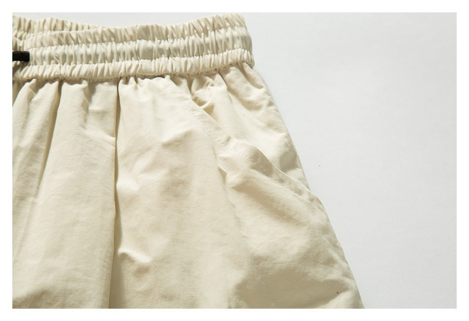 Close-up of cream-beige trousers showing a gathered elastic waistband and slanted side pocket.