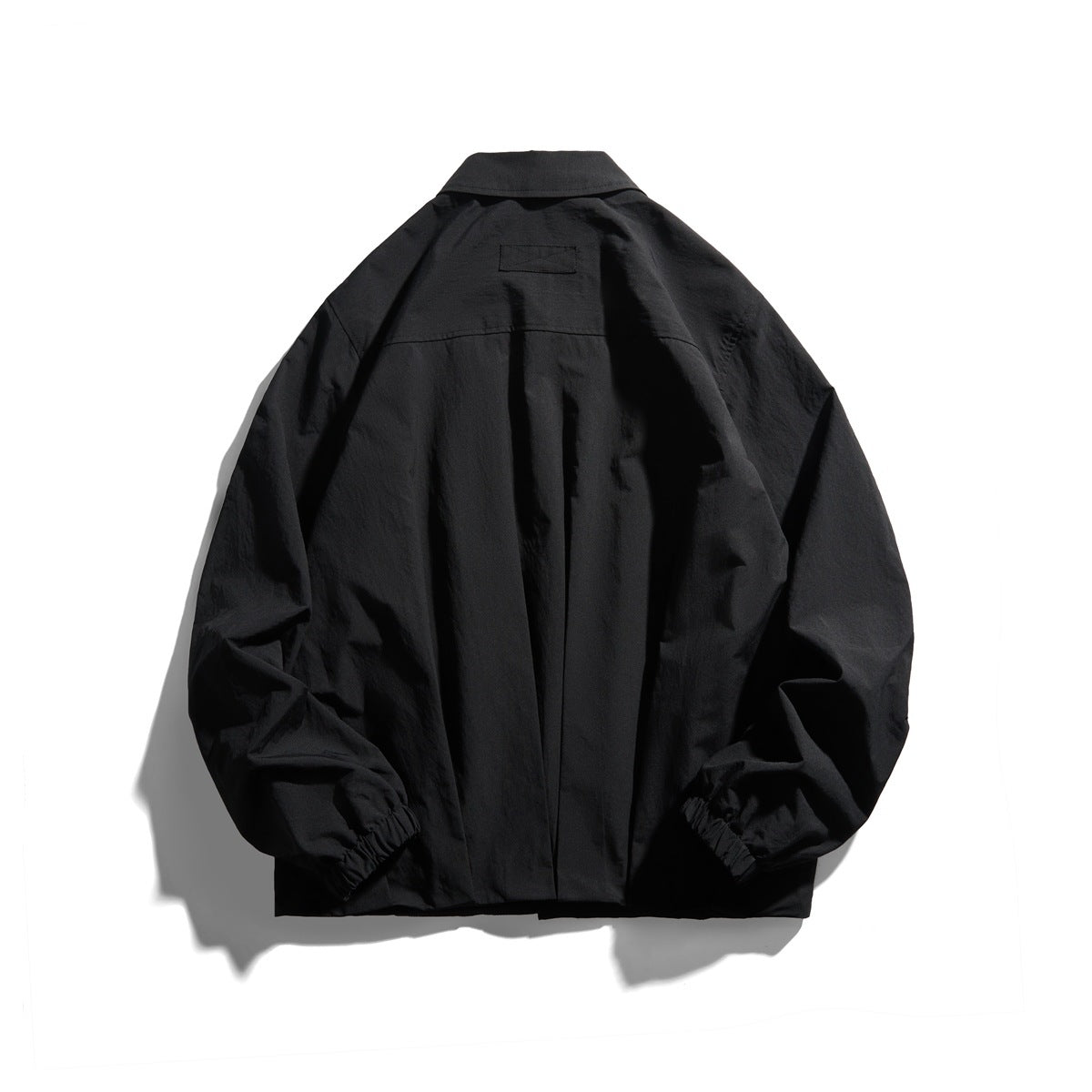 Back view of a black collared jacket with a shoulder yoke, center seam, and elastic cuffs.
