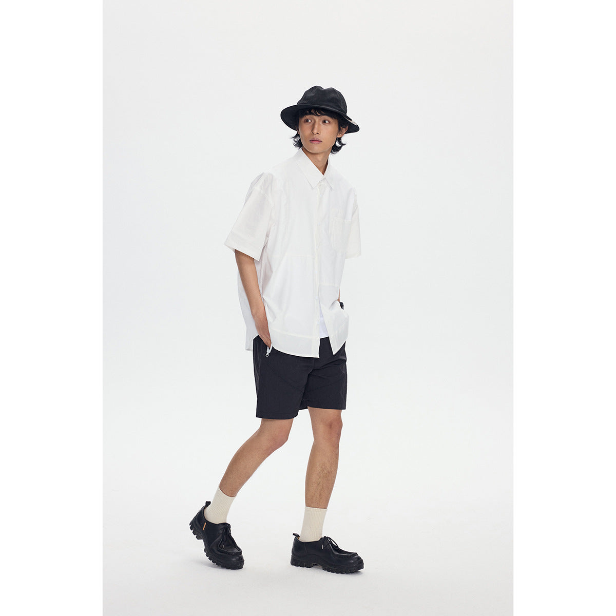 Model wearing a loose white short-sleeve button-up shirt and black shorts with a black bucket hat.