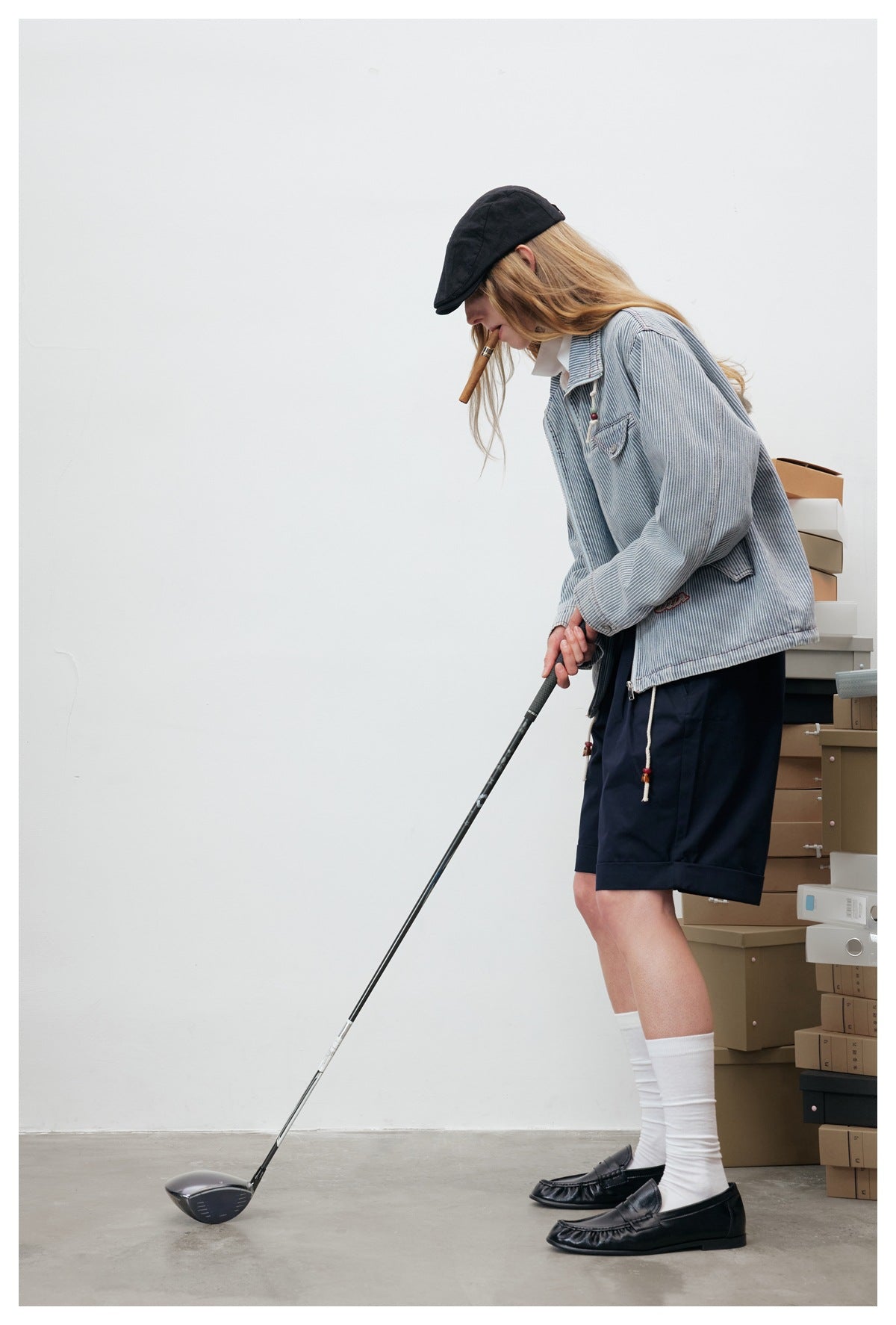 Side view of a model wearing the pinstriped jacket and navy shorts while holding a golf club.