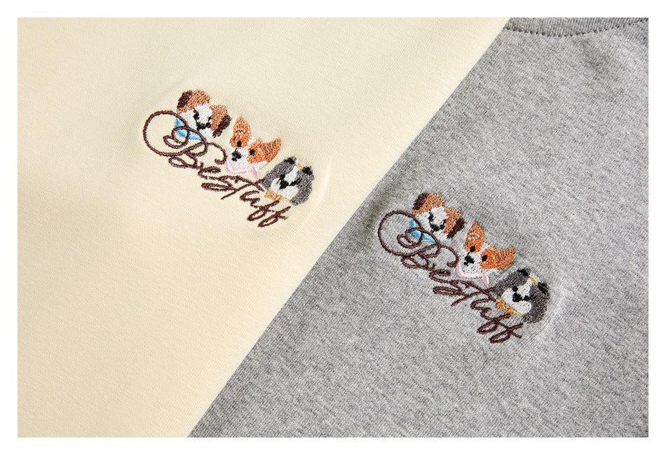 Close-up of cream and gray garment fabric, each embroidered with small cartoon cats and cursive lettering.