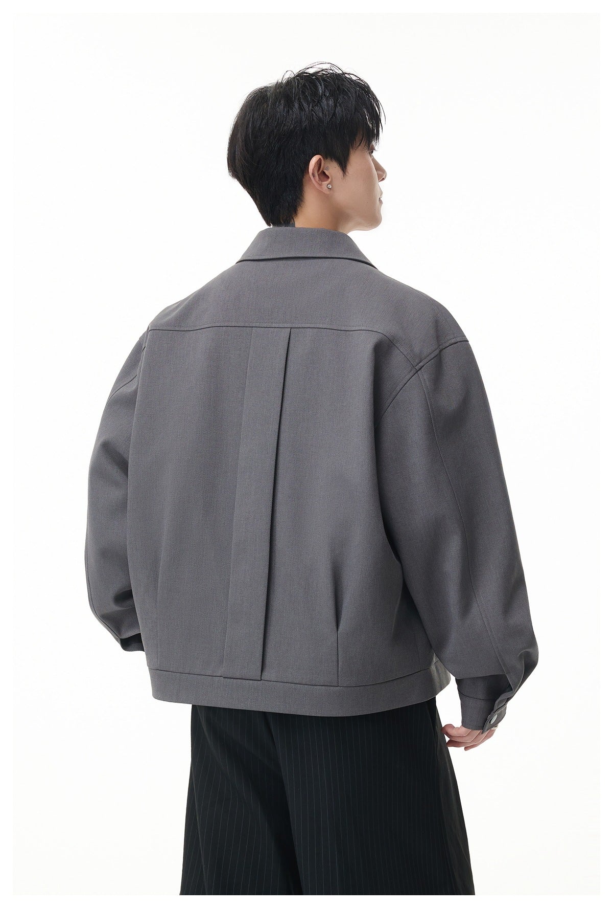 Rear view of a model wearing a gray jacket with a center back pleat and broad shoulder yoke.