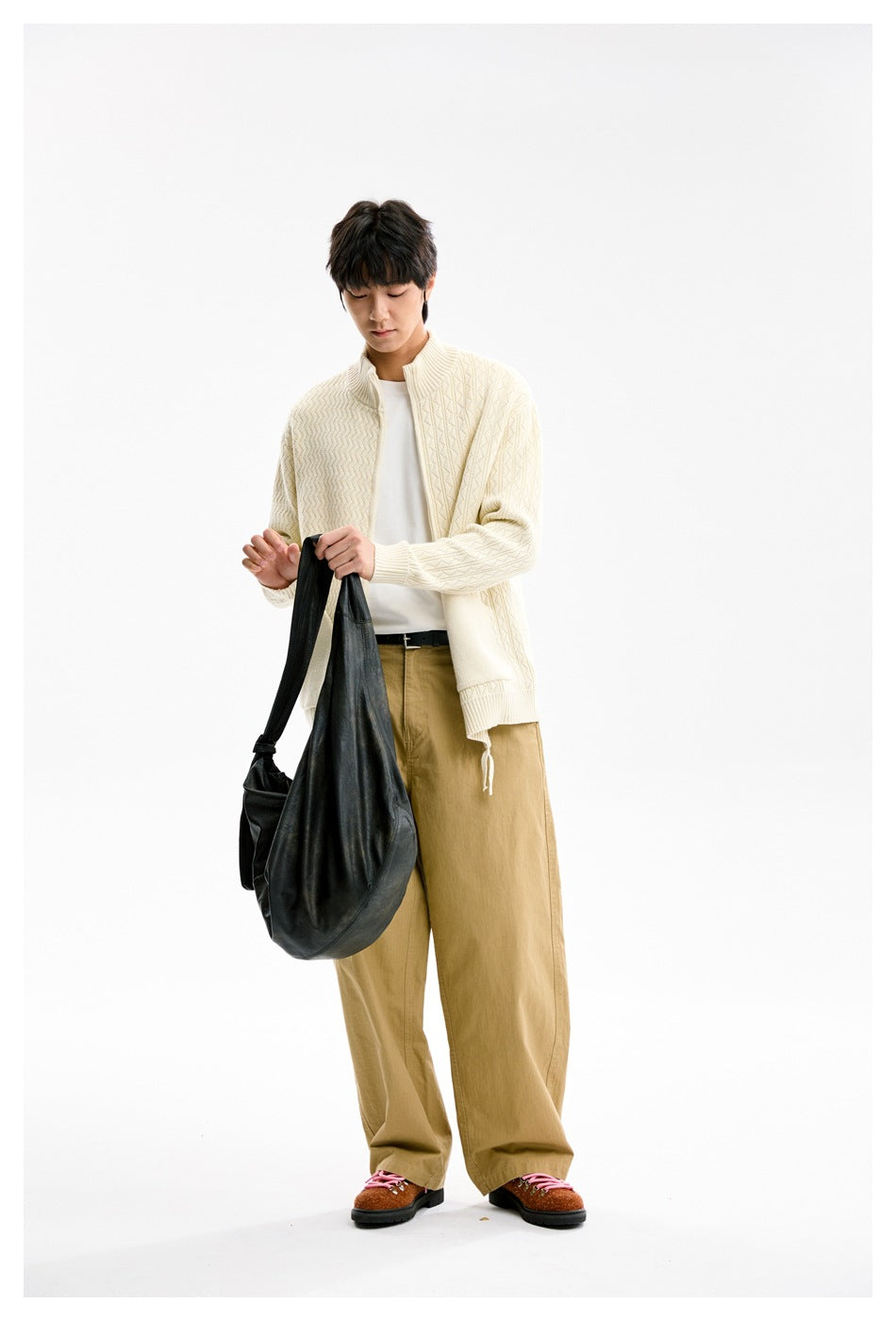 Model looking down wearing apricot textured knit zip cardigan with white tee and khaki pants, holding a black bag