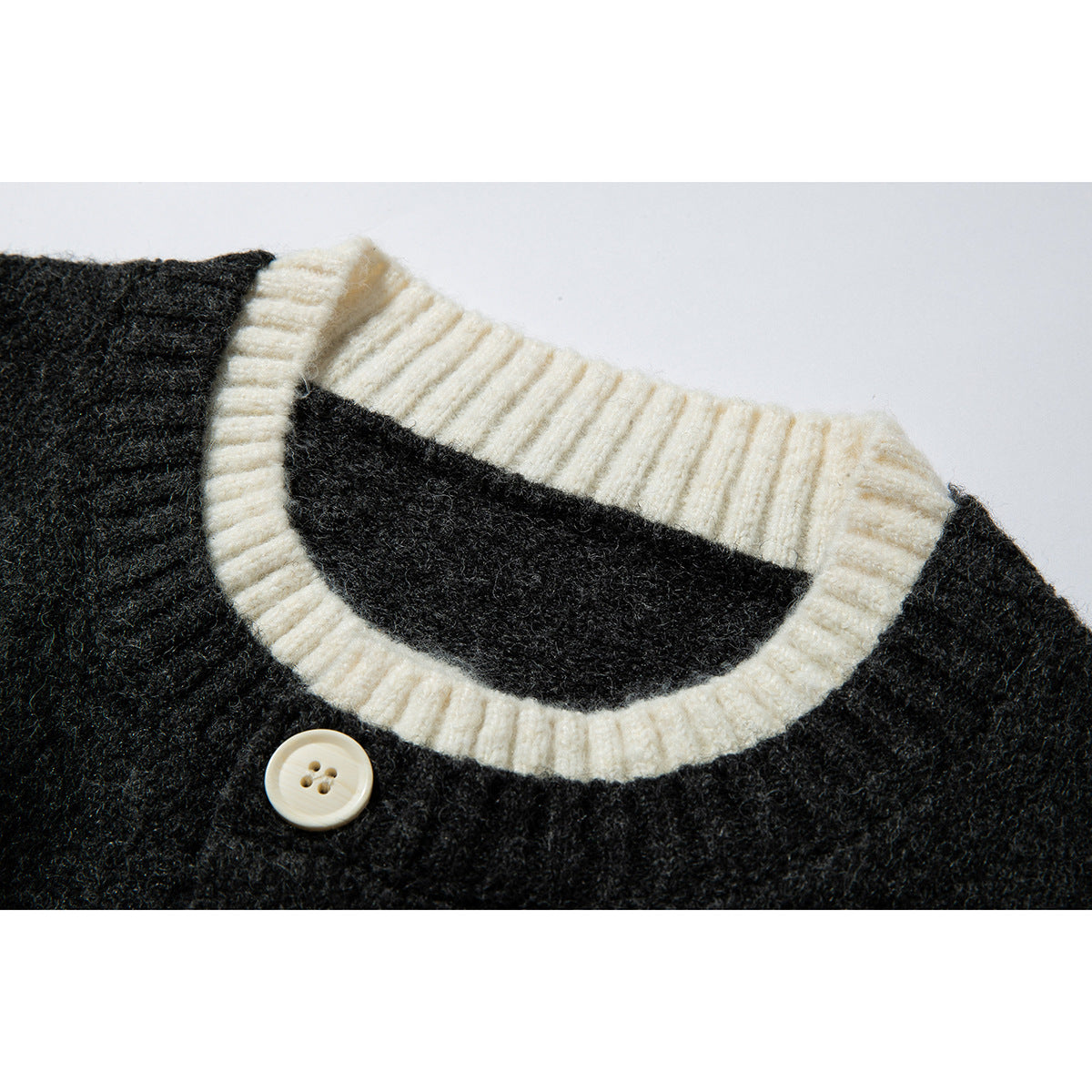 Close-up of a charcoal knit cardigan neckline with cream ribbed trim and a cream four-hole button.