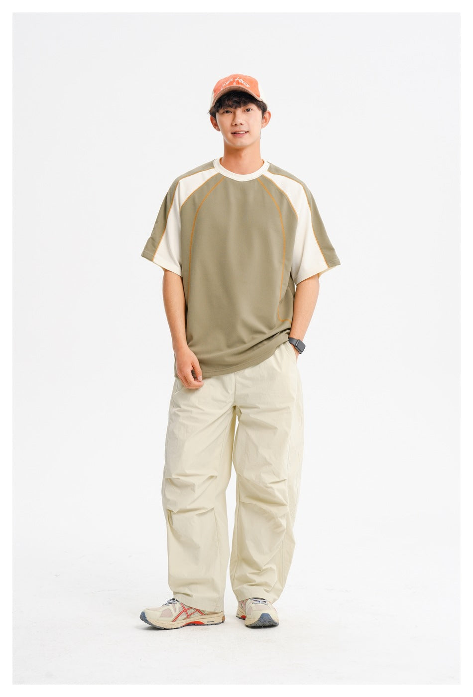 Model wearing green and cream raglan T-shirt with orange stitching, beige wide-leg pants and an orange cap