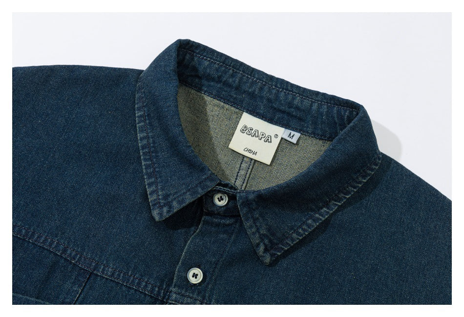 Framed close-up of a dark indigo denim shirt collar, buttons, and sewn neck label.