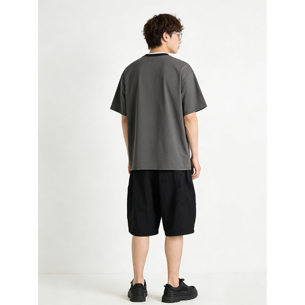 Back view of a model wearing a dark charcoal T-shirt with a contrasting collar and black shorts.
