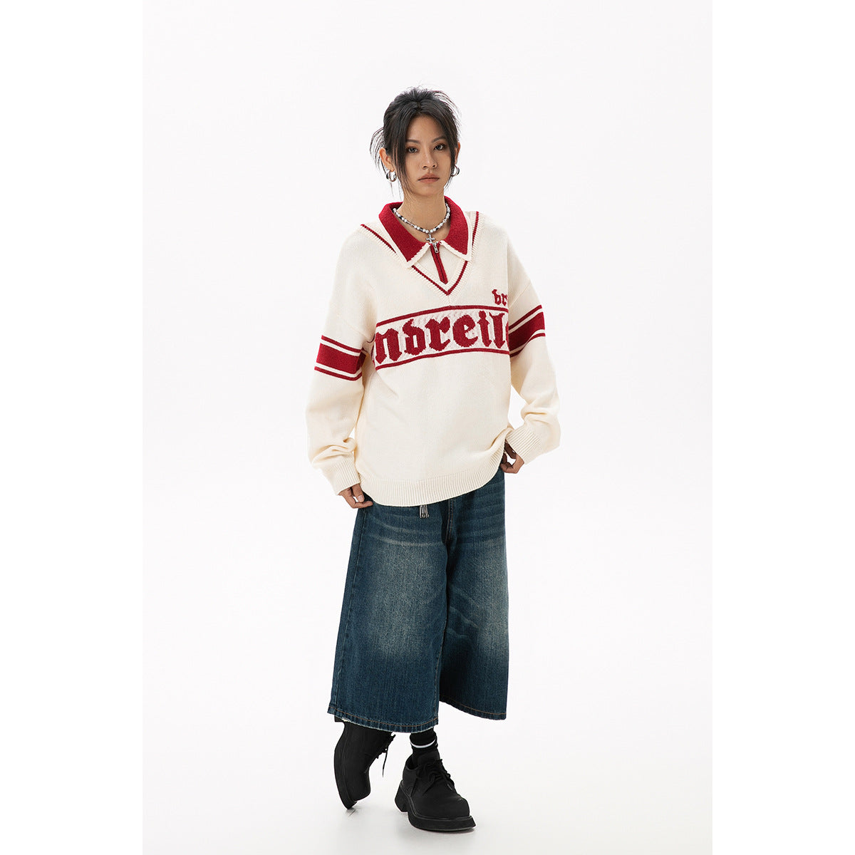 Model wearing an ivory sweater with red collar, sleeve stripes and chest lettering, paired with wide-leg denim shorts.