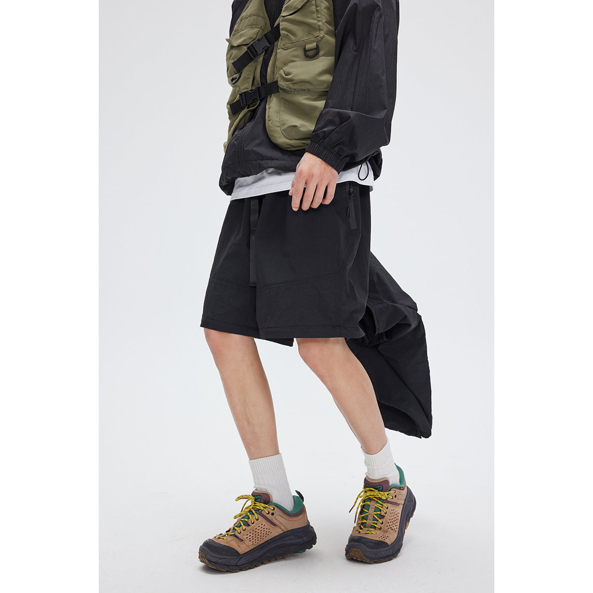 Side view of a model wearing black shorts with the detached pant legs hanging behind.