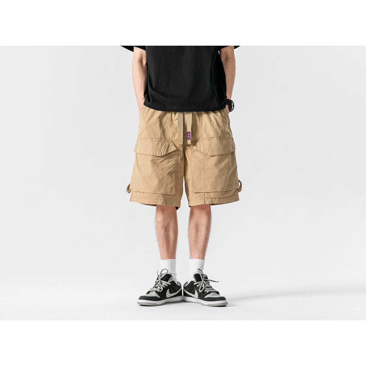 Front view of a model wearing tan cargo shorts with large flap pockets and a black T-shirt.