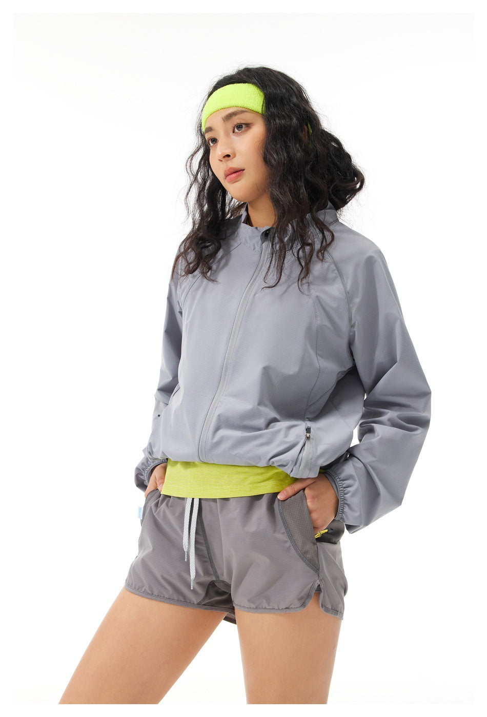 Model wearing a gray zip jacket and matching shorts with a neon yellow top and headband.