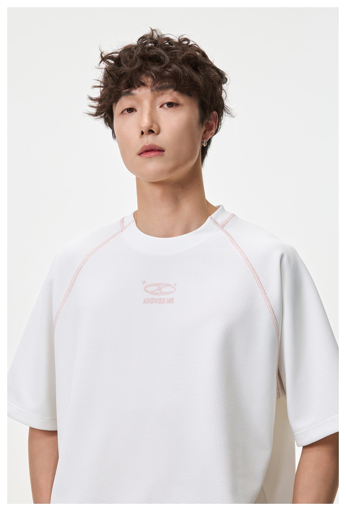 Close front view of a model wearing a white textured raglan T-shirt with pale pink piping and a small chest graphic.